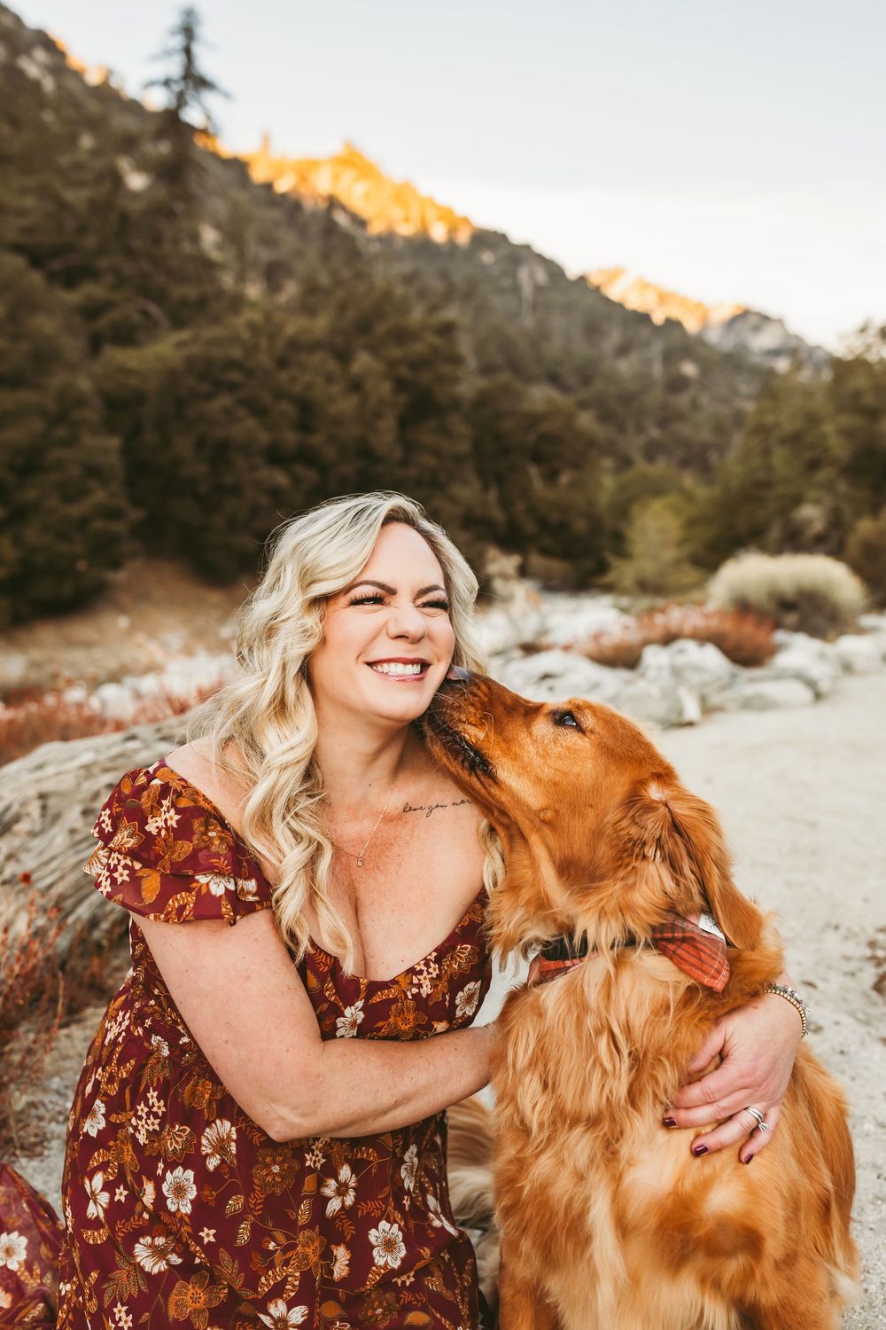 A joyful moment shared between a woman in a floral dress and a golden retriever against a mountain backdrop.
