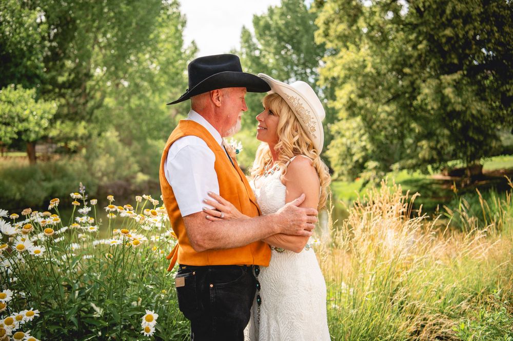 A couple embraces in a garden setting with wildflowers and tall grasses during a golden hour photoshoot.
