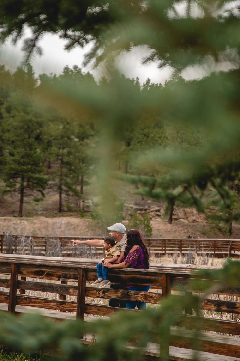 Two people sitting together on wooden benches at an outdoor amphitheater surrounded by pine trees on a cloudy day.