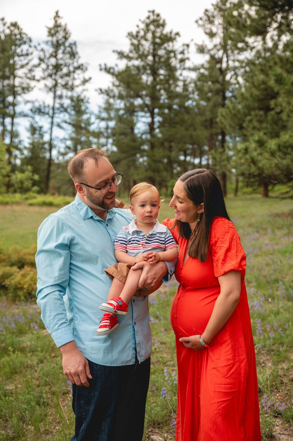 A family wearing blue and red outfits shares joyful moments together in a scenic outdoor setting with pine trees.