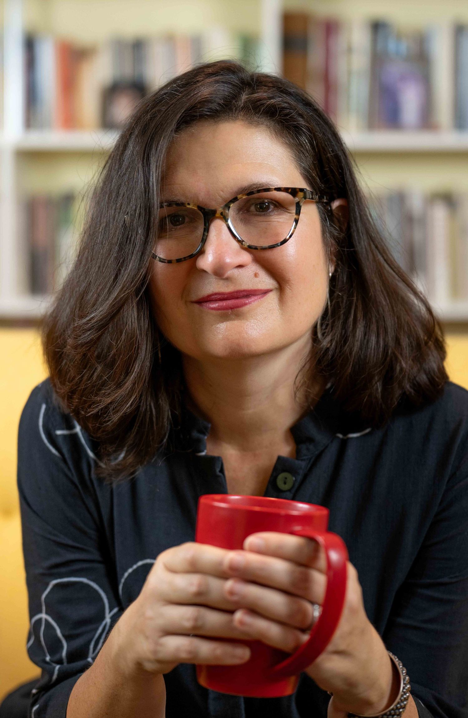 A casual portrait of someone holding a red coffee mug in front of a bookshelf.