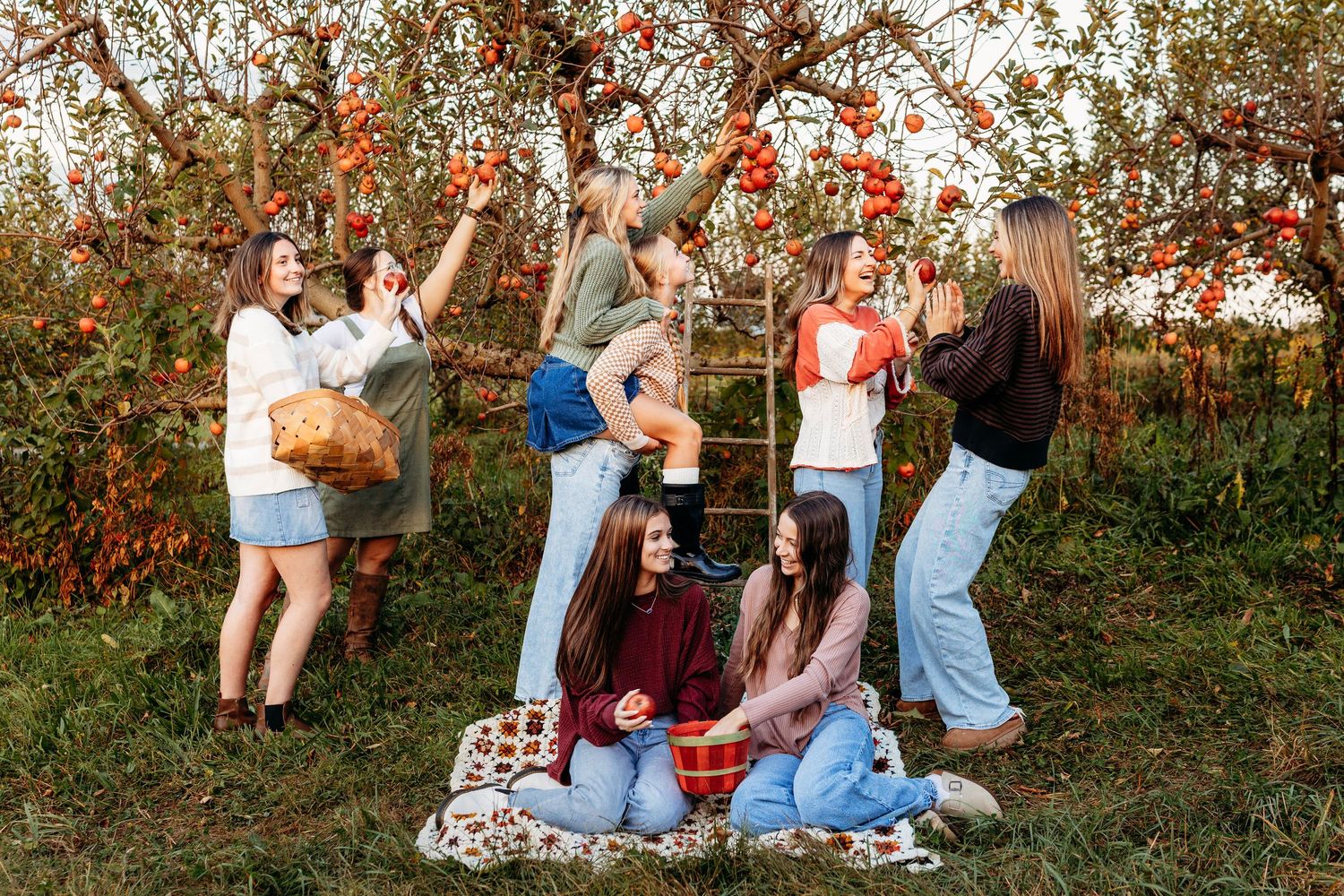 Group of young women picking red apples from trees in an autumn orchard setting.