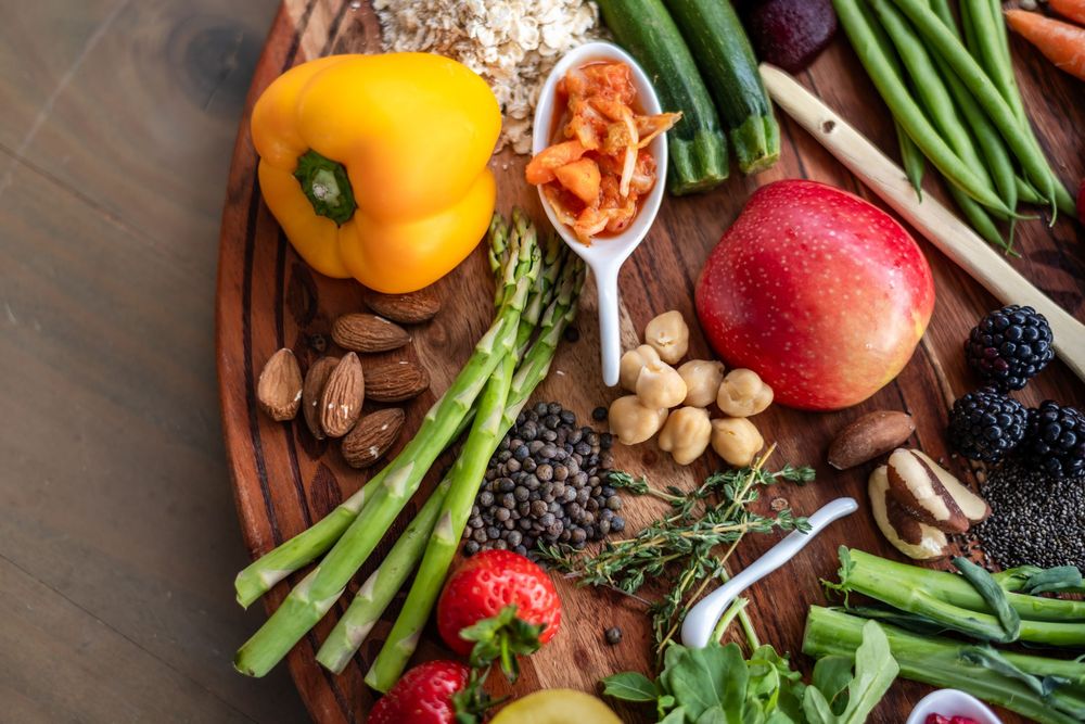 Fresh produce and healthy ingredients including vegetables, fruits, nuts and grains arranged on a wooden surface.