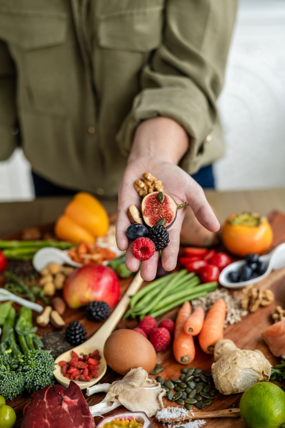 Hand holding fresh berries over a table filled with colorful fruits, vegetables, nuts and healthy ingredients.