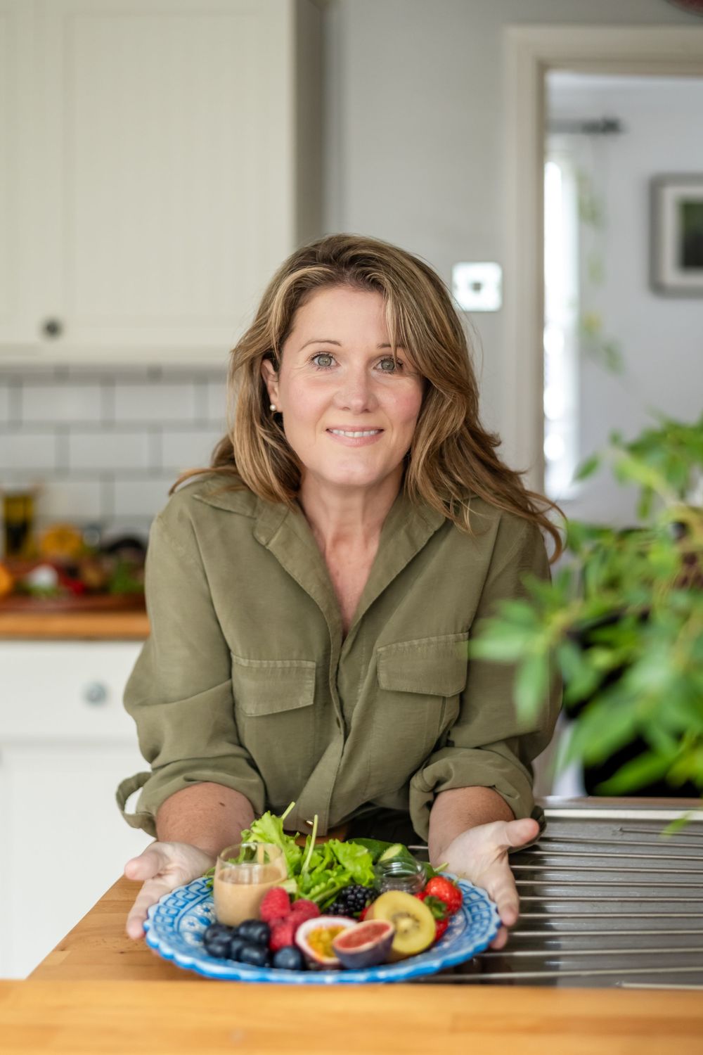 Person in olive green shirt leaning on wooden table with healthy food and produce arranged on blue plate.