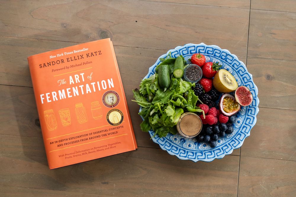 Orange cookbook and fresh produce arranged on wooden surface with blue and white patterned plate.