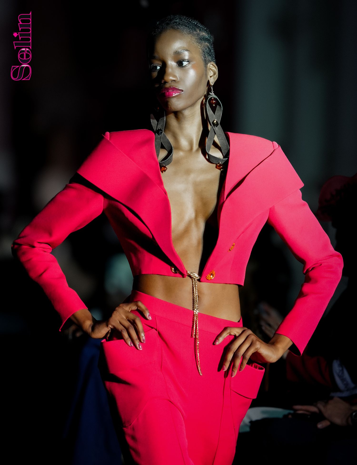 A model walks the runway in a striking red cutout dress with structured shoulders and long sleeves.