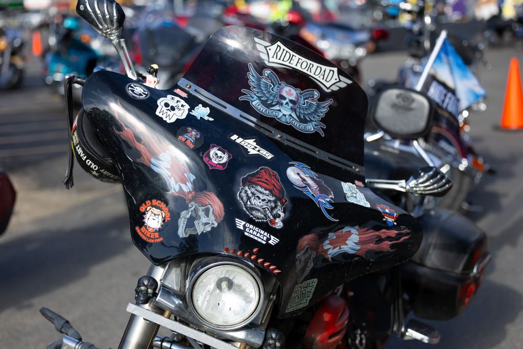 Row of parked motorcycles with chrome and black finishes lined up at an outdoor event or gathering.