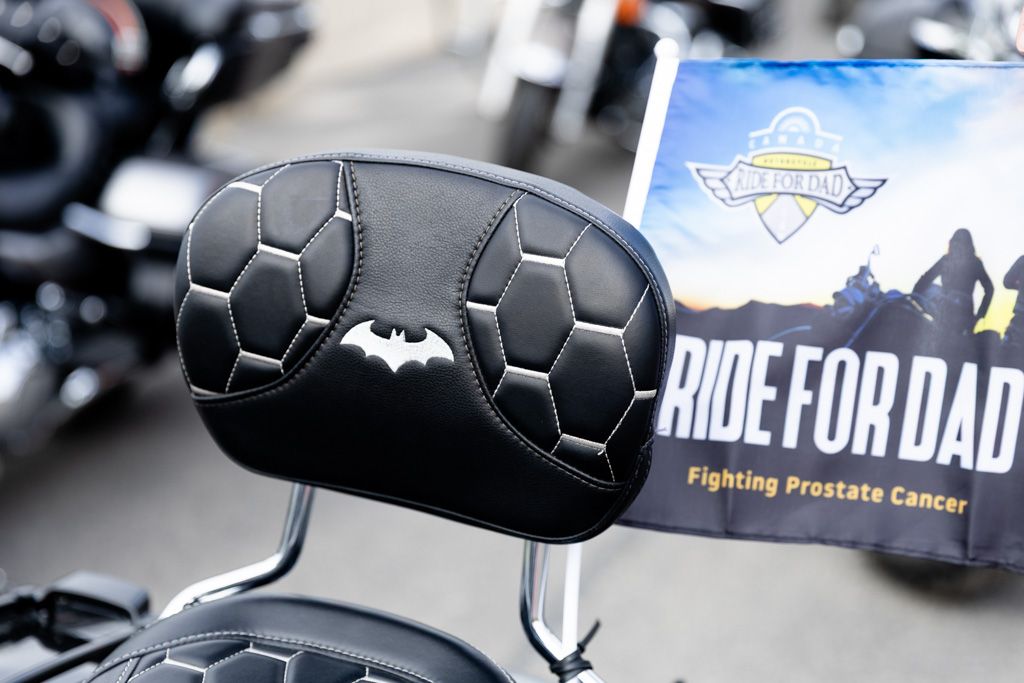 A row of black motorcycle handlebars with custom grips lined up at a prostate cancer awareness motorcycle event.
