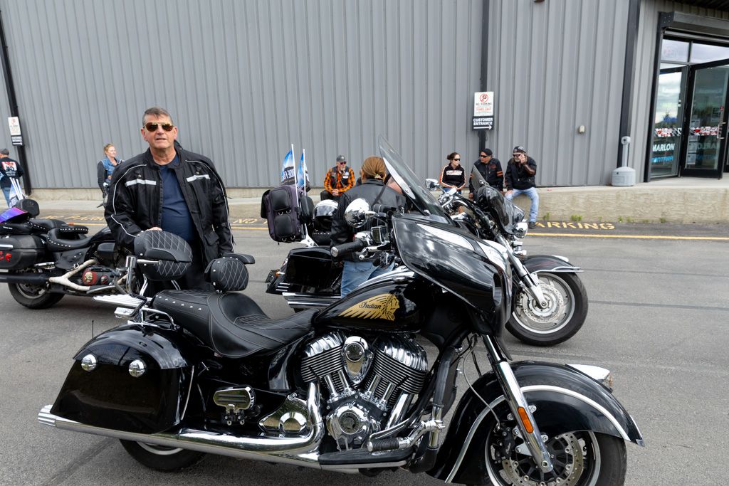 Motorcycles lined up in a row outside a gray industrial building on a sunny day.