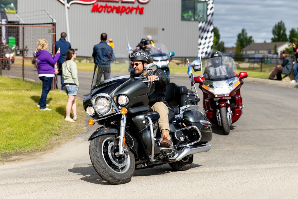 Motorcycles parked in a row on a paved lot with green grass and buildings in the background.