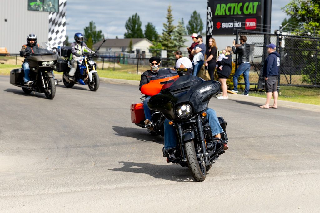 Motorcycles lined up in a parking lot during a sunny day with riders gathering for a group event.