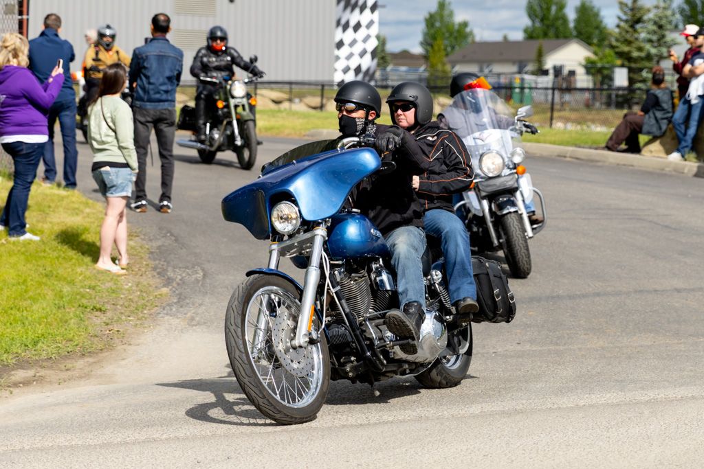 Row of parked motorcycles with riders gathered at a motorcycle dealership event.