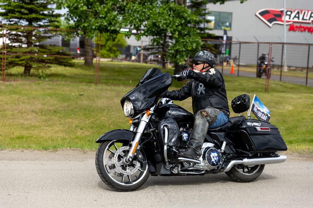 Multiple motorcycles parked in front of Ralph's Motorsports building with green trees in background.