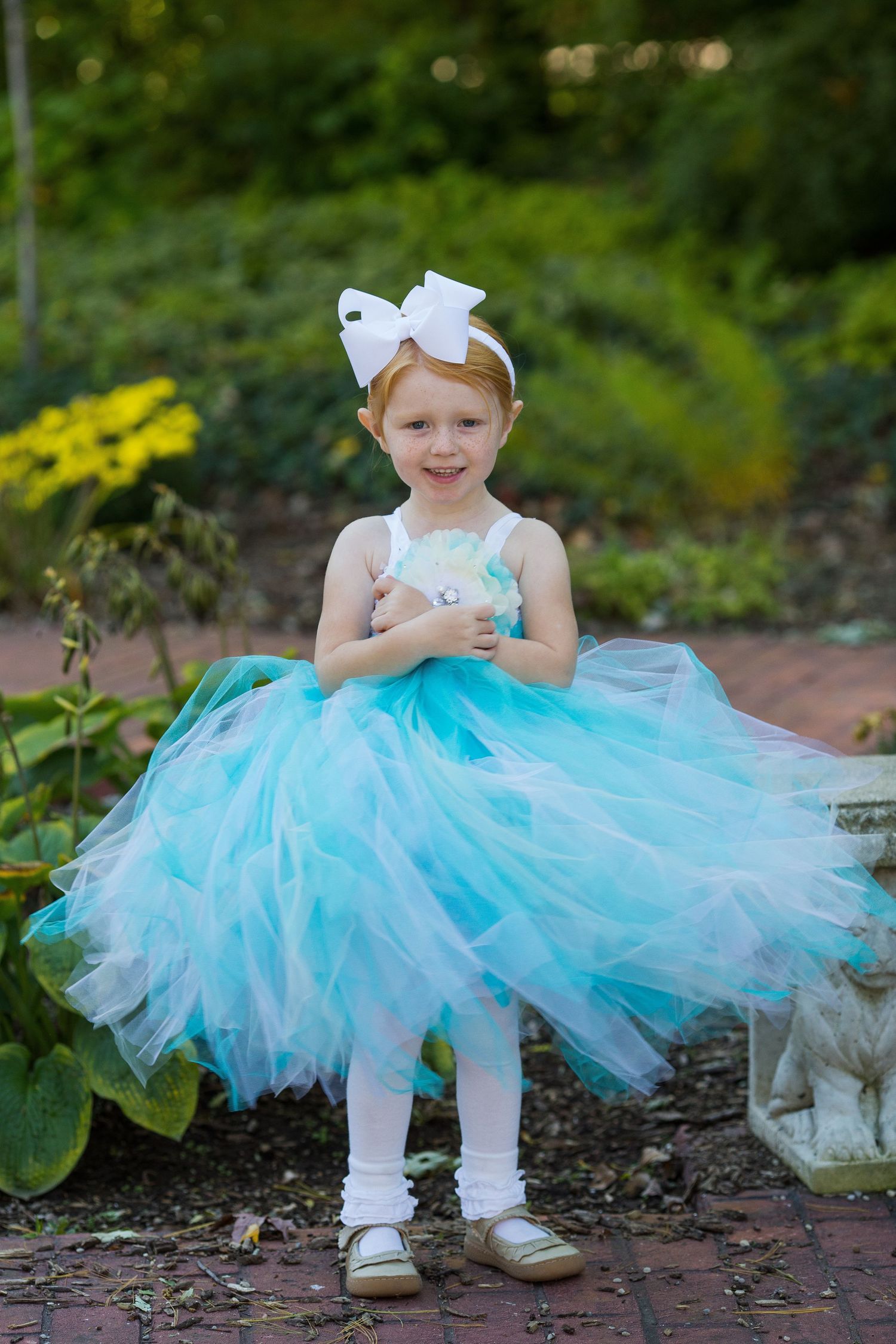 A young dancer in a turquoise tulle dress poses in a garden setting.
