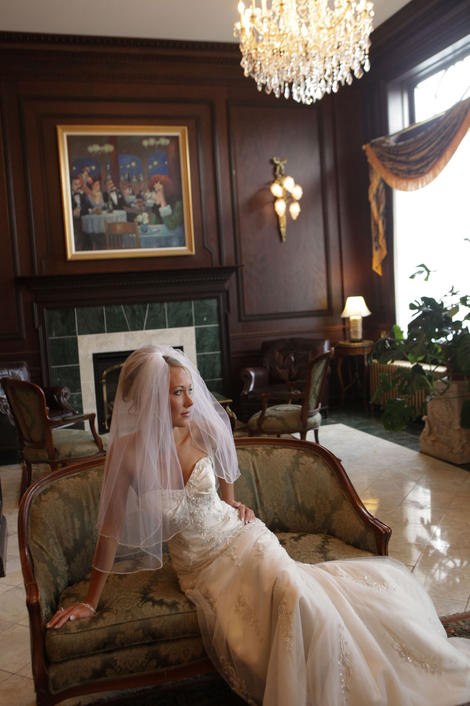 A wedding dress flows gracefully across an antique chaise lounge beneath a crystal chandelier.