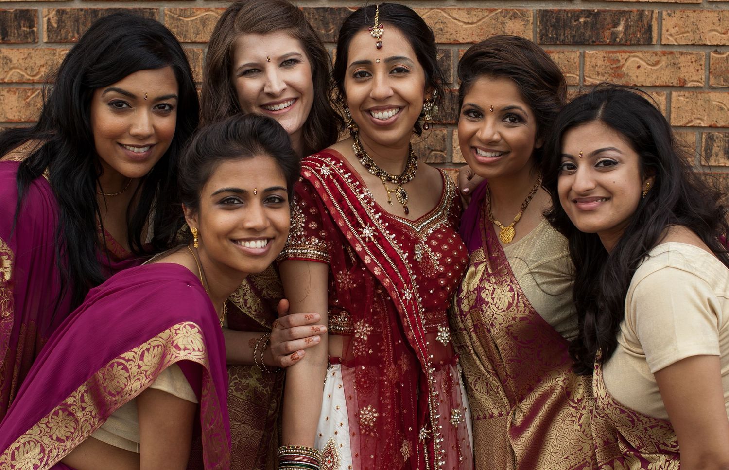 A group of women in traditional Indian and western attire smile together at a cultural celebration event.