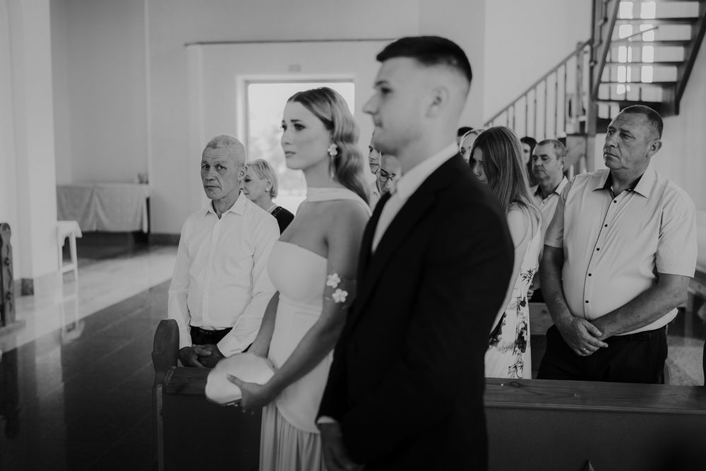 A black and white photo capturing a wedding ceremony with attendees watching in a church setting.