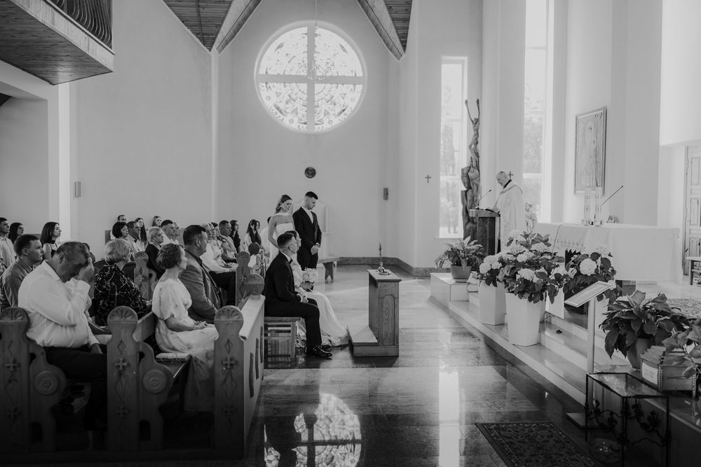 Black and white photo of church interior with guests seated during a wedding ceremony.