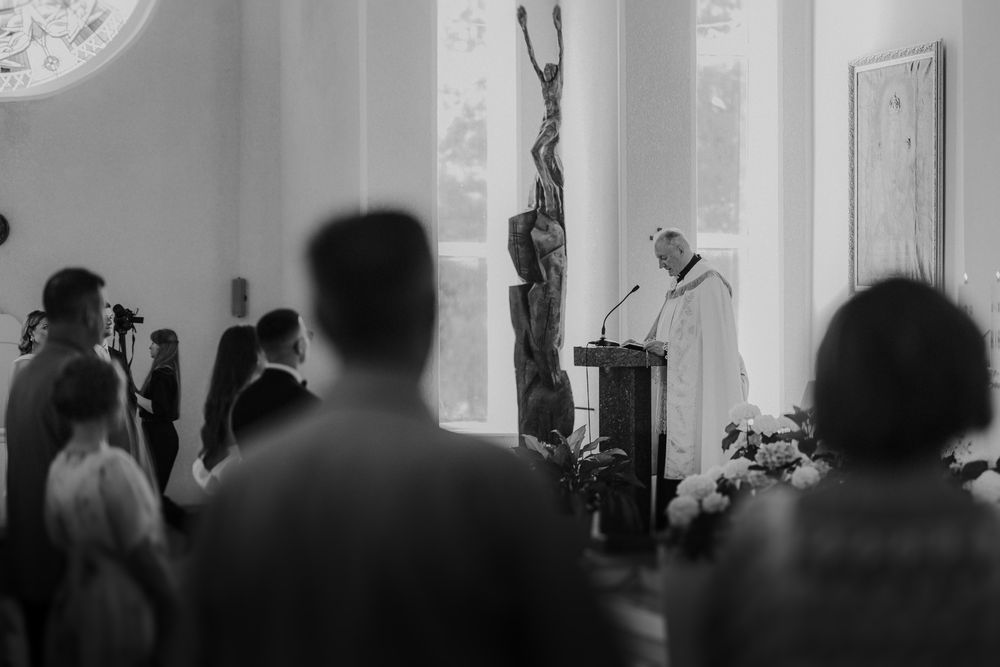 Silhouettes of wedding guests in a bright white church interior.