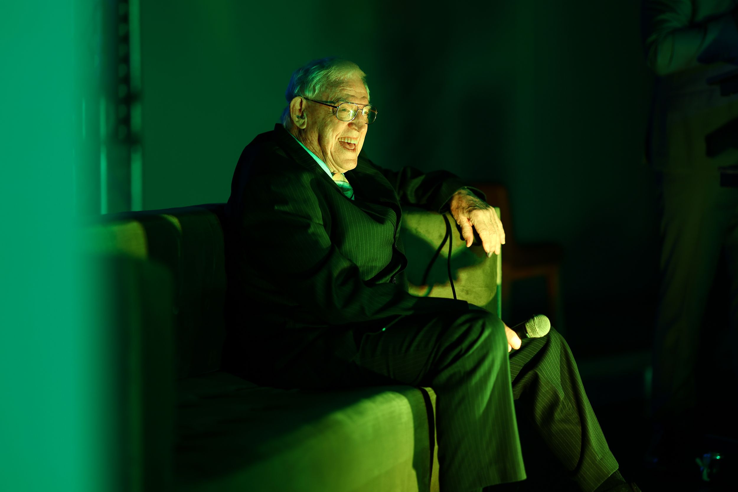 Person illuminated by dramatic green lighting while seated in a dark room.