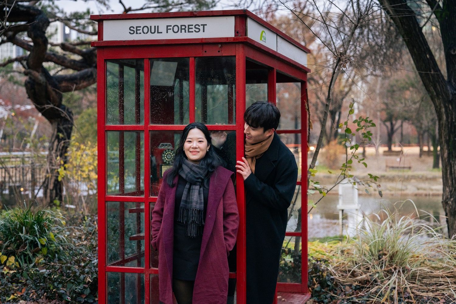 People stand near red phone booths in Seoul Forest park during autumn season.