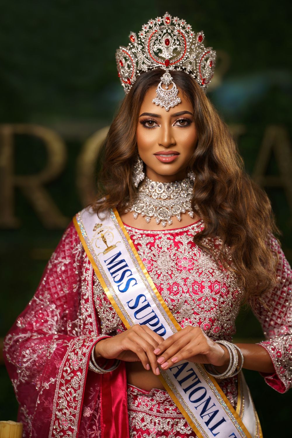 Beauty pageant contestant wearing an ornate silver crown and pink embellished gown with traditional Indian jewelry.