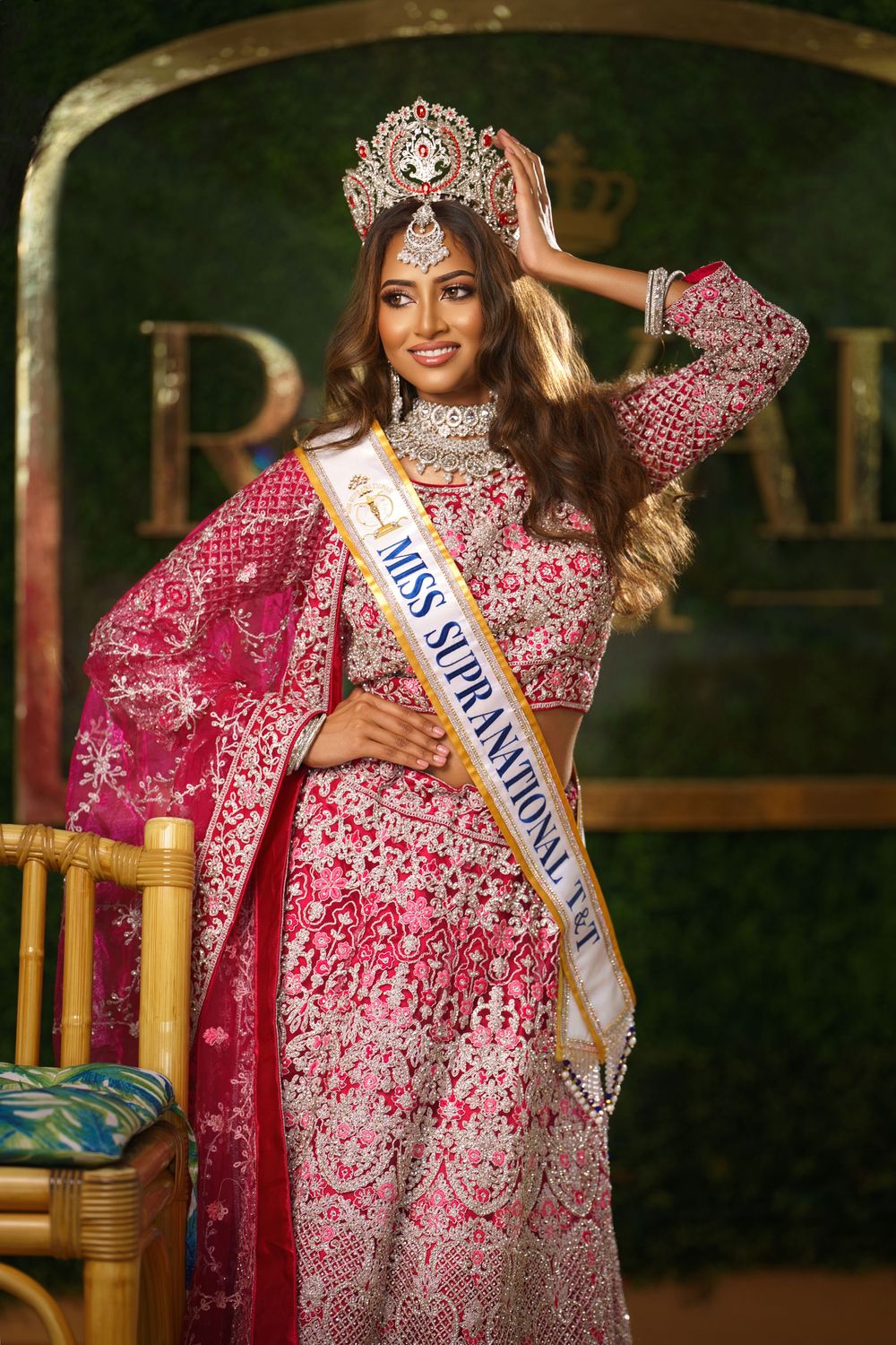 Beauty pageant contestant wearing an ornate pink and silver embellished gown with traditional crown and sash poses elegantly.