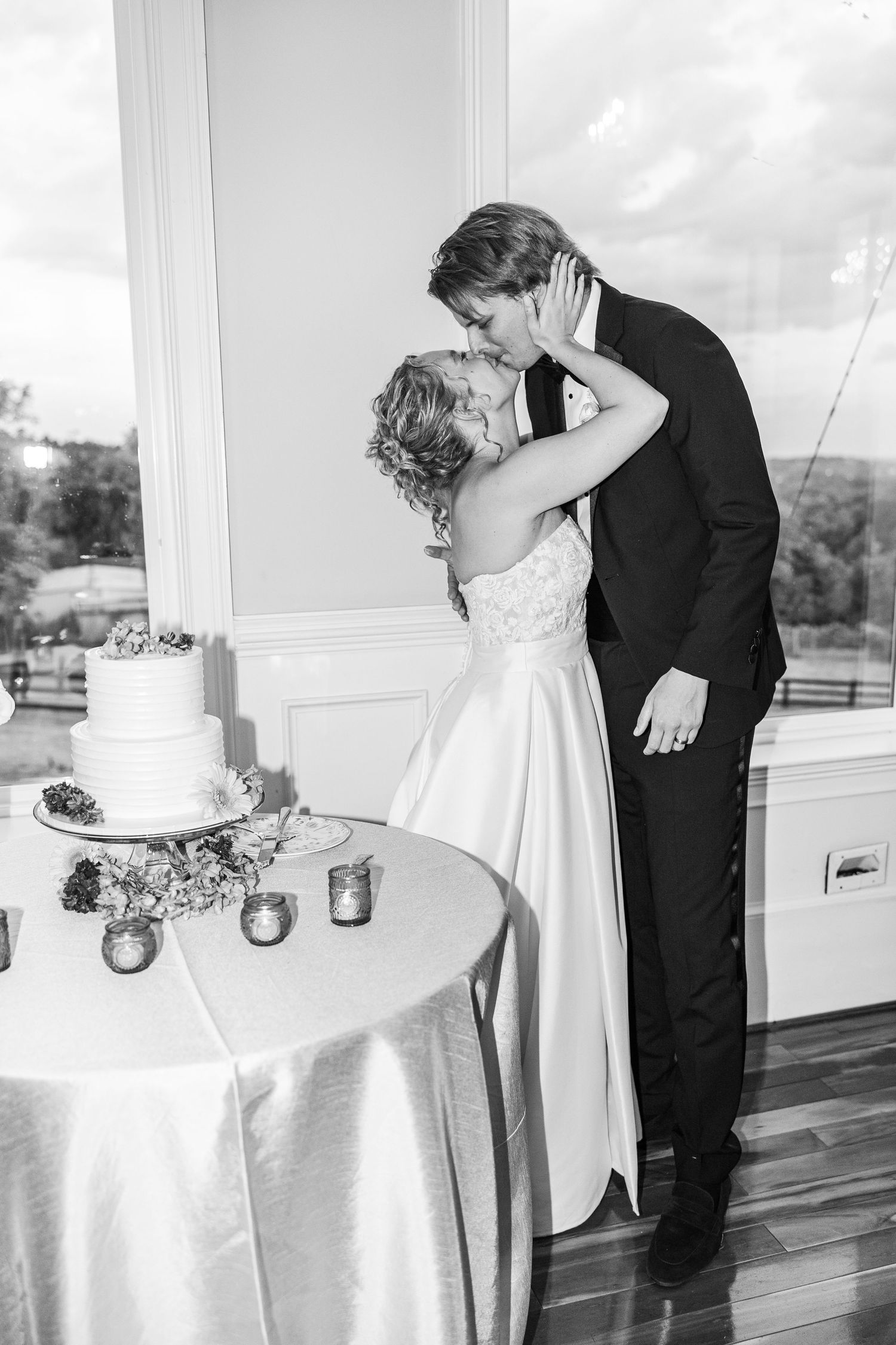 A romantic black and white wedding moment captured next to an elegant tiered cake.