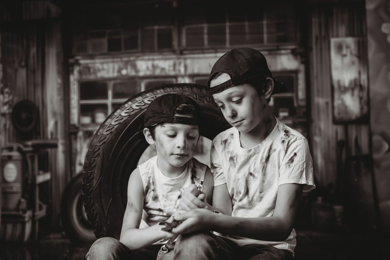Two children in vintage clothing share a moment while sitting together in a black and white photograph.