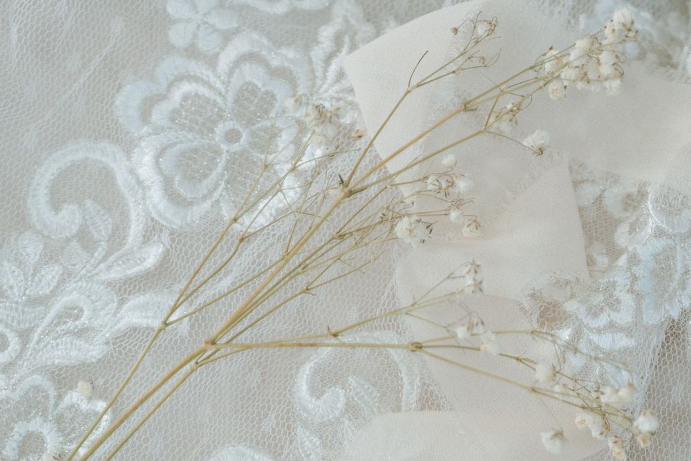 Delicate dried baby's breath flowers laying on white lace fabric with embroidered floral pattern.