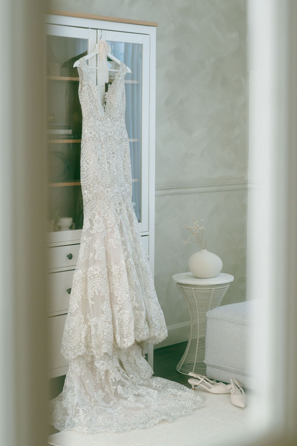 A white lace wedding dress hangs elegantly in front of a mirror, creating a beautiful reflection in a bridal boutique.