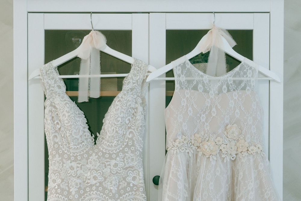Elegant white wedding dresses displayed on hangers in a bridal boutique with delicate lace and beaded details.
