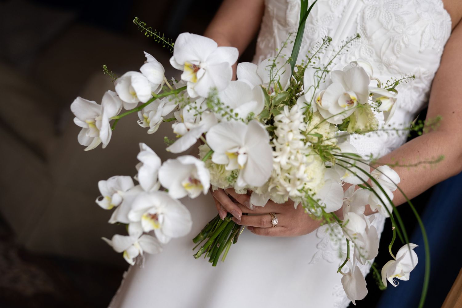 Elegant white orchid and baby's breath wedding bouquet against neutral background.