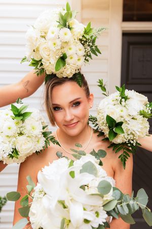Smiling bride surrounded by multiple white floral bouquets with roses and greenery. Little Wren Rockwall, Texas. Dallas Fort Worth Wedding
