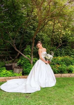Bride in a strapless white ballgown with long train holds bouquet in a lush garden setting. The Little Wren Rockwall, TX. DFW Wedding