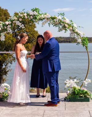 A small outdoor wedding ceremony takes place on a lake with a floral arch and scenic lake view in the background. Eagle Mountain Fort Worth