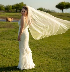 Bride in a fitted lace gown poses in a field with her flowing veil catching the wind. Fort Worth Dallas Texas wedding. Bridal portraits