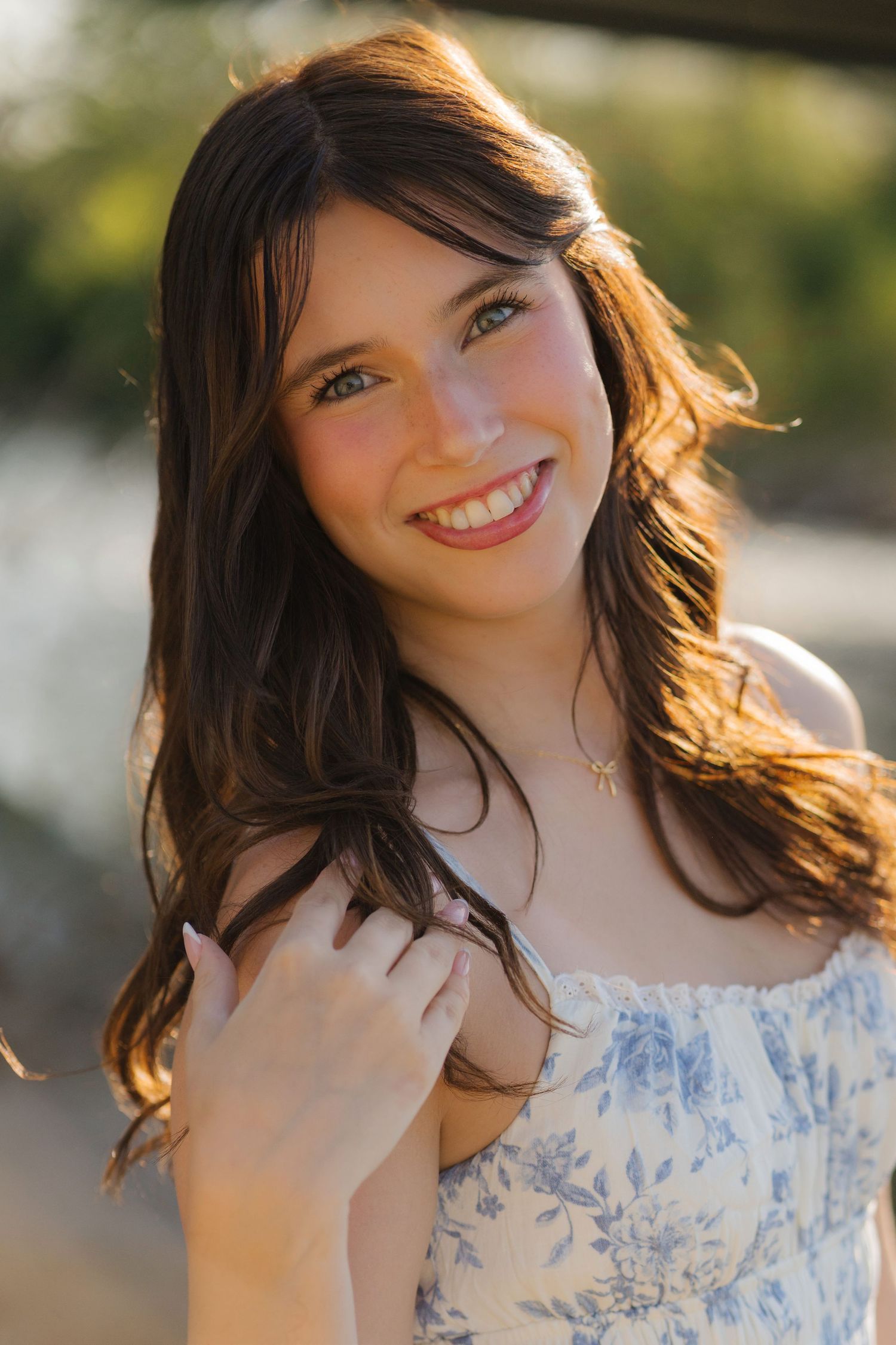 Portrait of person with long dark hair wearing floral dress outdoors in warm natural lighting.