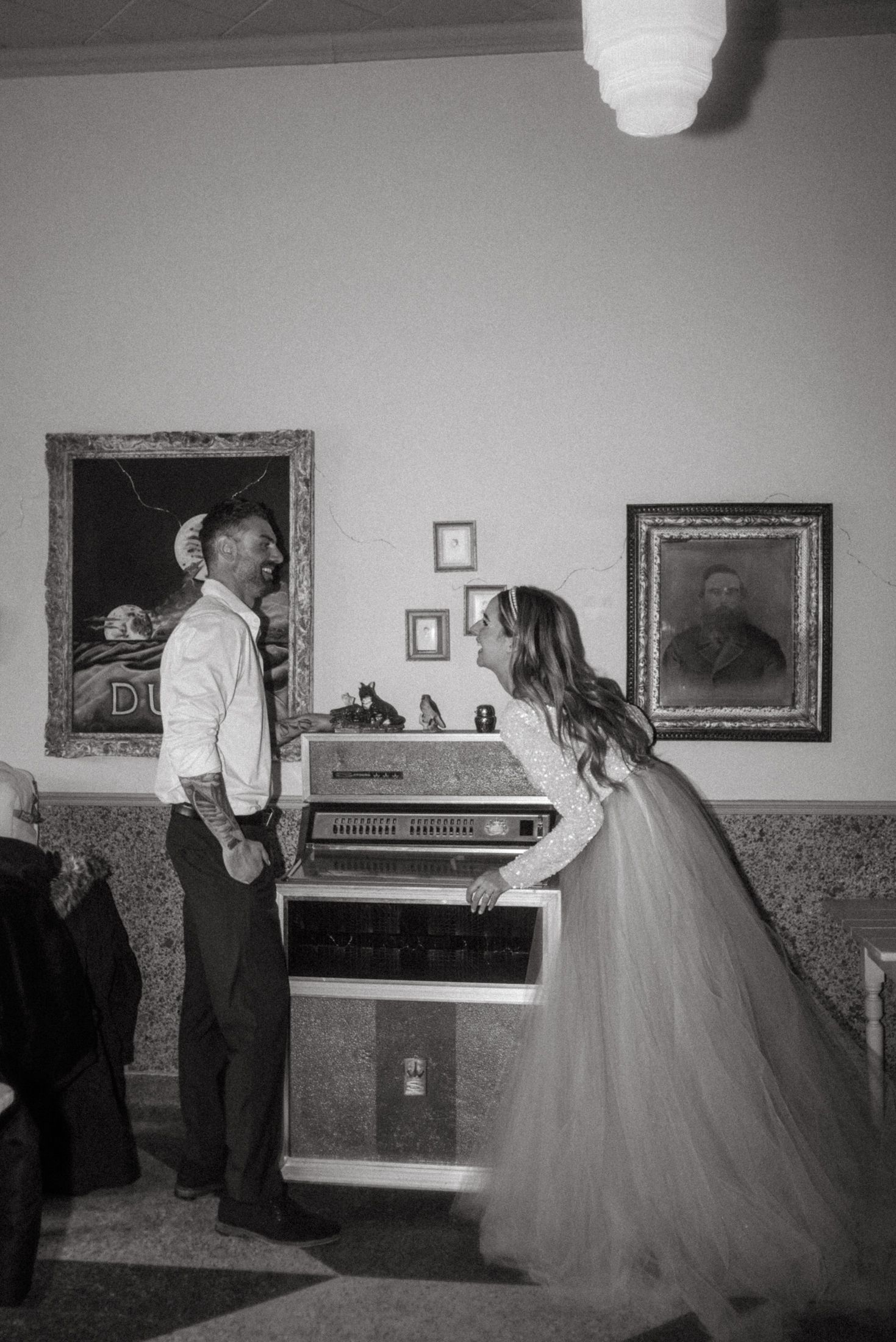 Couple poses near vintage jukebox in black and white photo.
