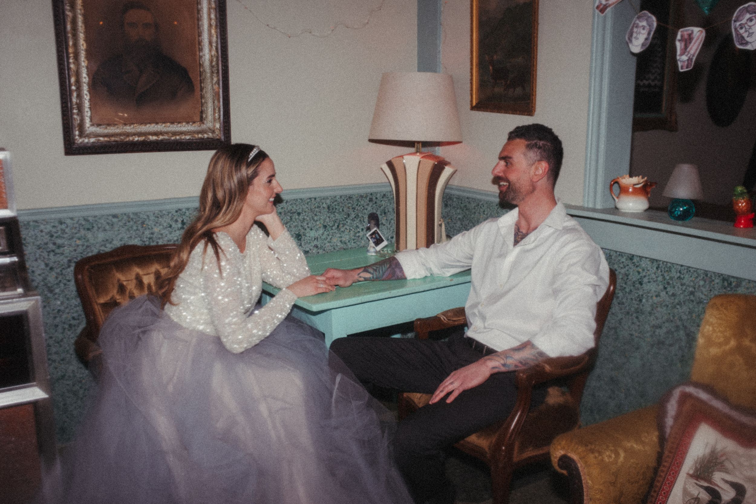 Couple in formal attire sits together in vintage-style lounge with antique decor.