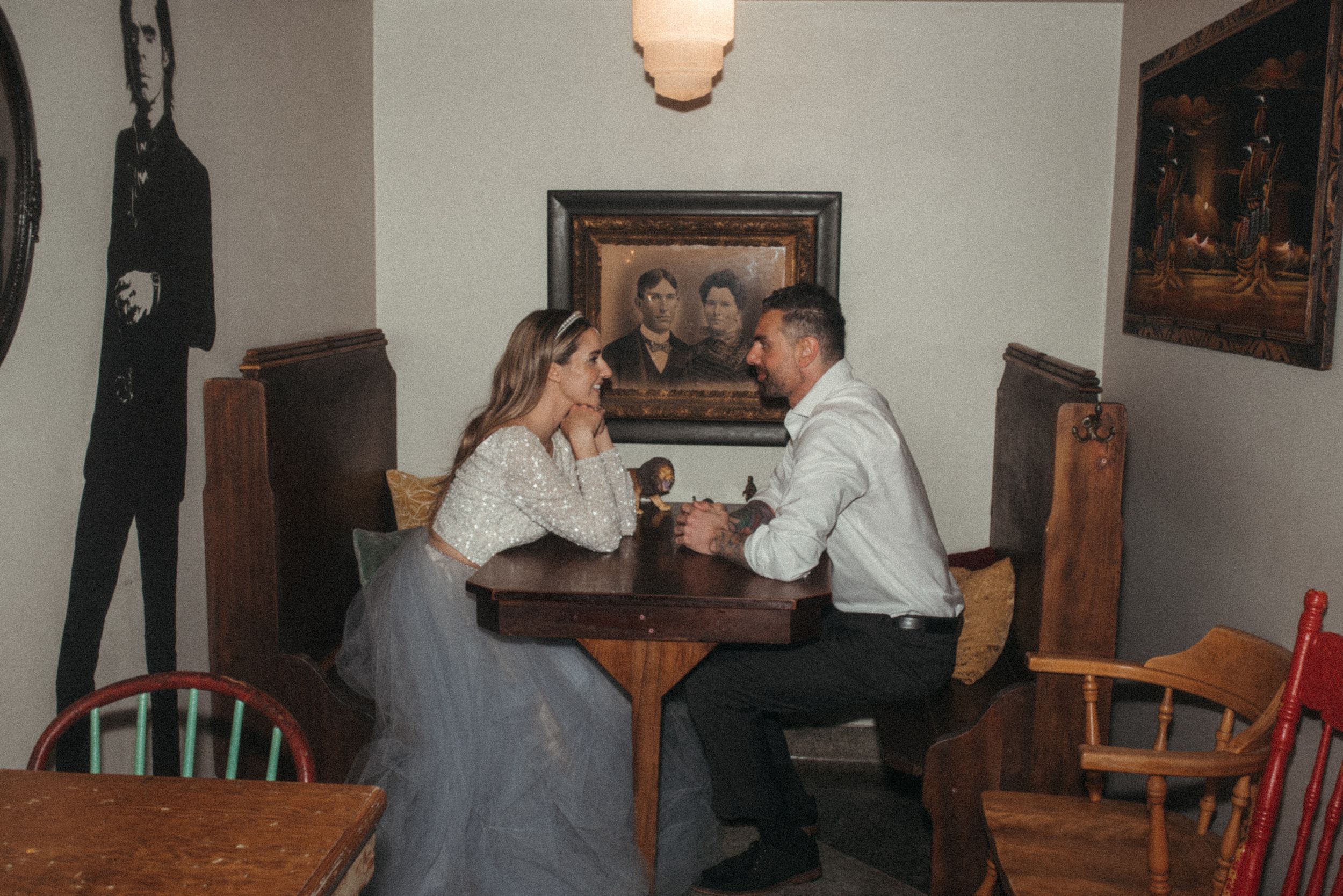 A couple sits at a wooden table in a retro-styled diner setting.