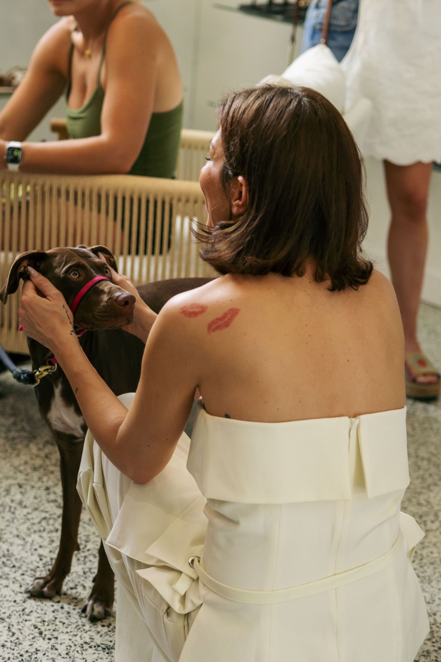 A woman with short brown hair petting a dog with both hands on the puppies face. She has a tattoo of red kisses on her shoulder.