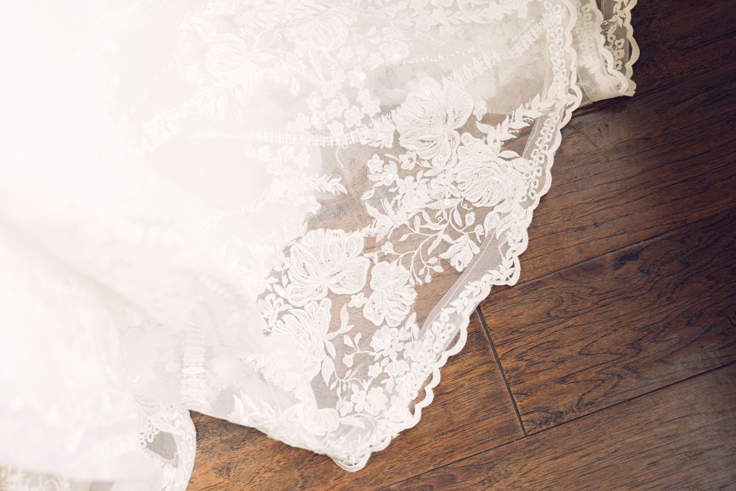 White lace wedding dress hem laying on dark hardwood flooring.