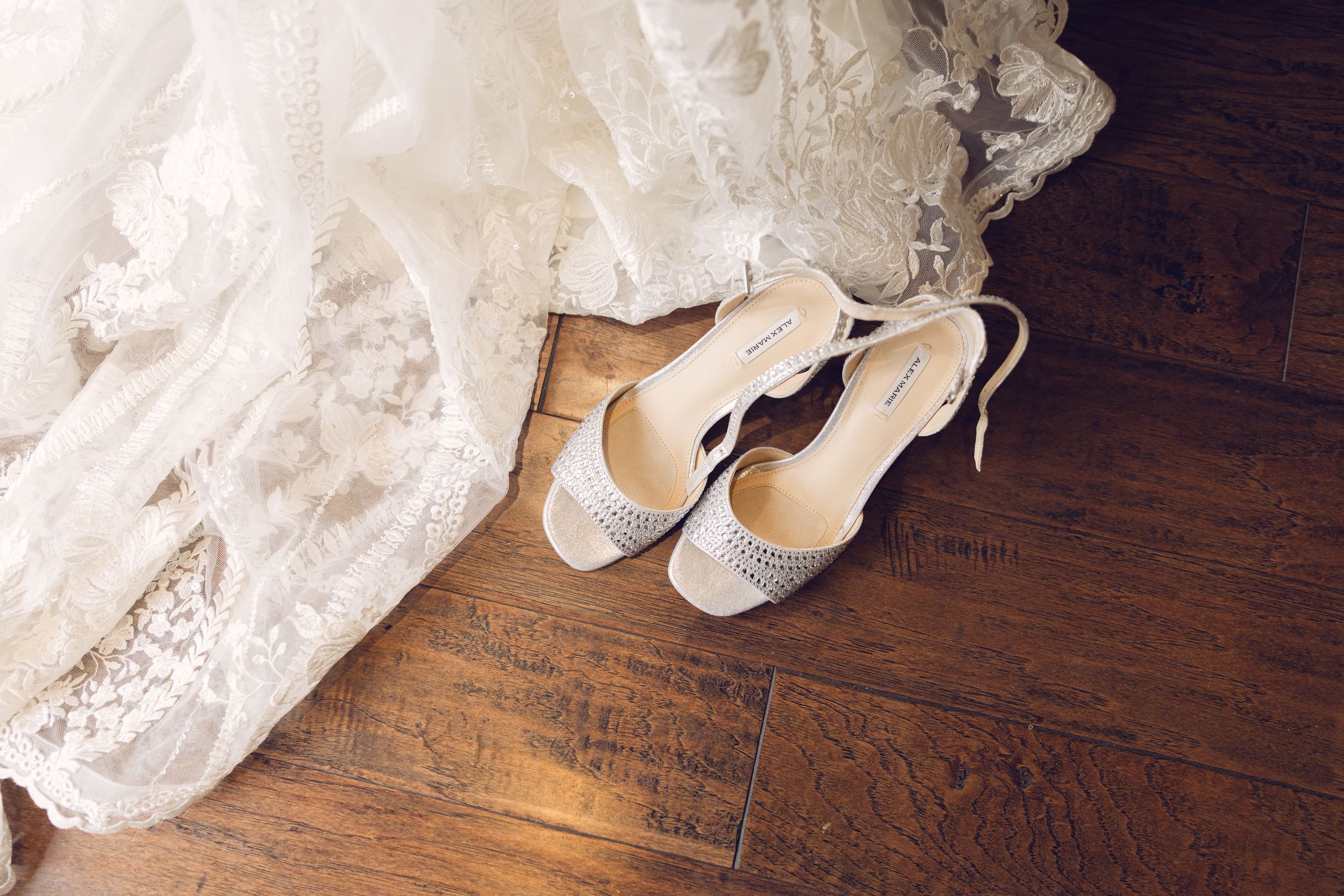 Wedding accessories including white shoes and lace dress on wooden floor.