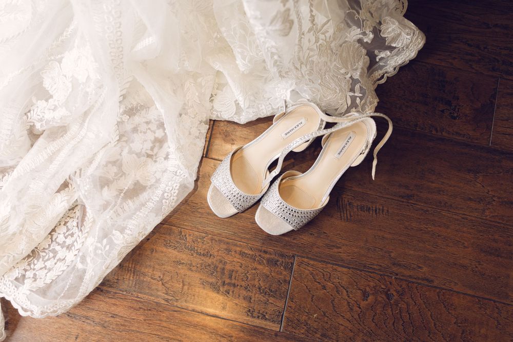 Wedding accessories including white shoes and lace dress on wooden floor.