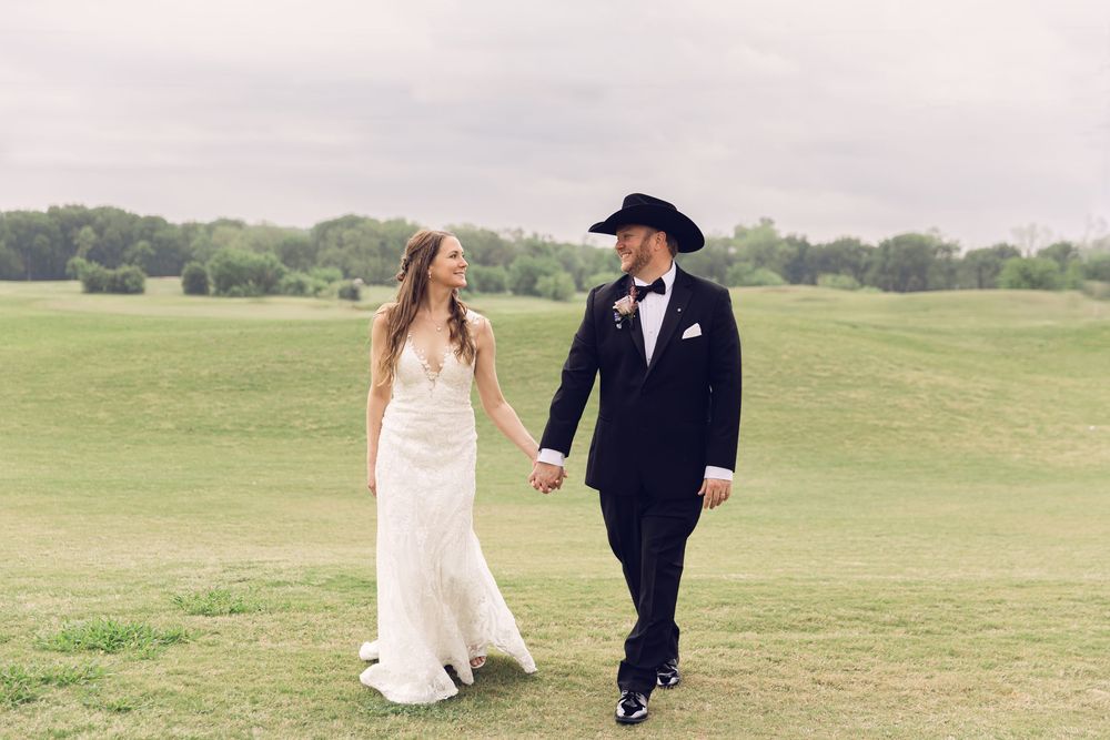 Wedding couple walking hand in hand across a scenic grassy field on their special day.