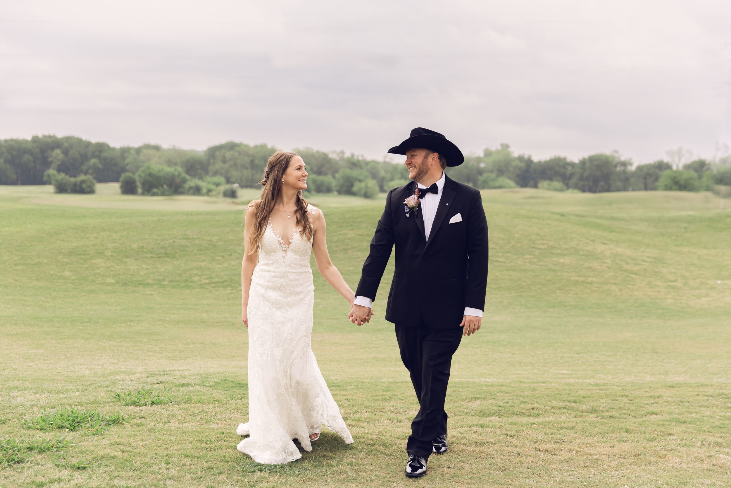 Wedding couple walking hand in hand across a scenic grassy field on their special day.