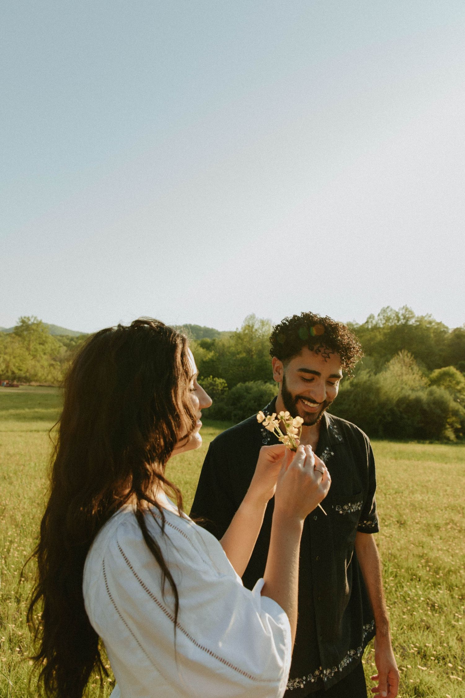 Couple shares playful moment with flowers in sunny meadow during golden hour.