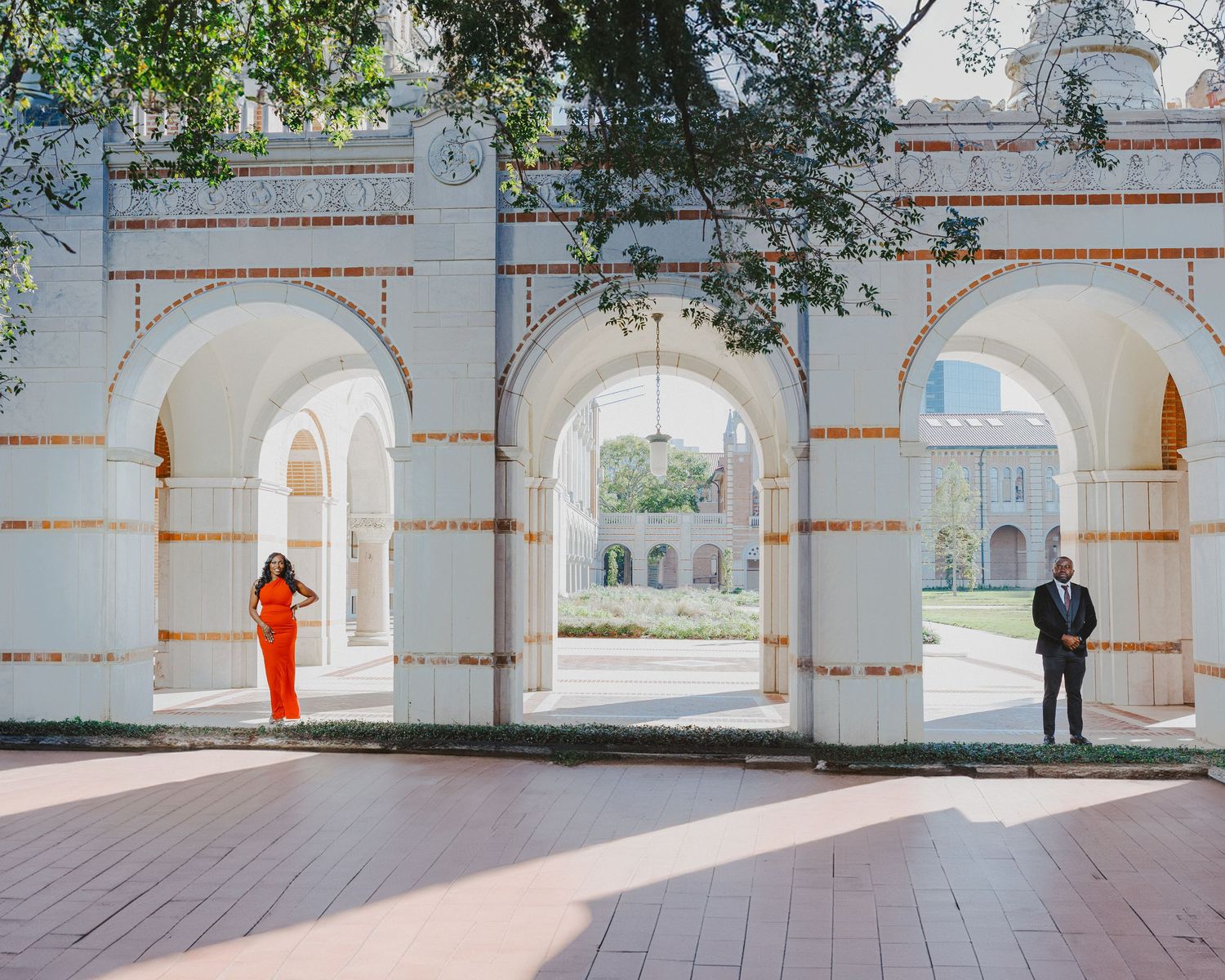 White architectural arches with two standing figures in an elegant colonial-style courtyard with afternoon light streaming through.